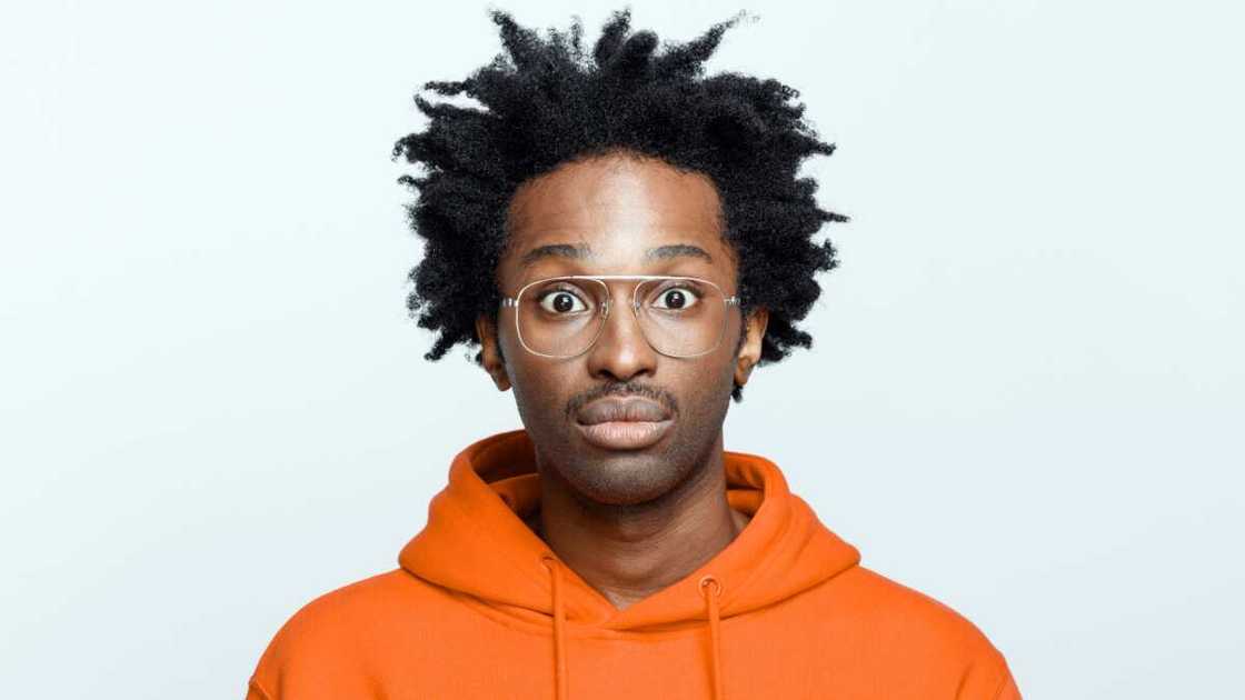 A young man wearing an orange hoodie and glasses staring at someone A young man wearing an orange hoodie and glasses staring at someone