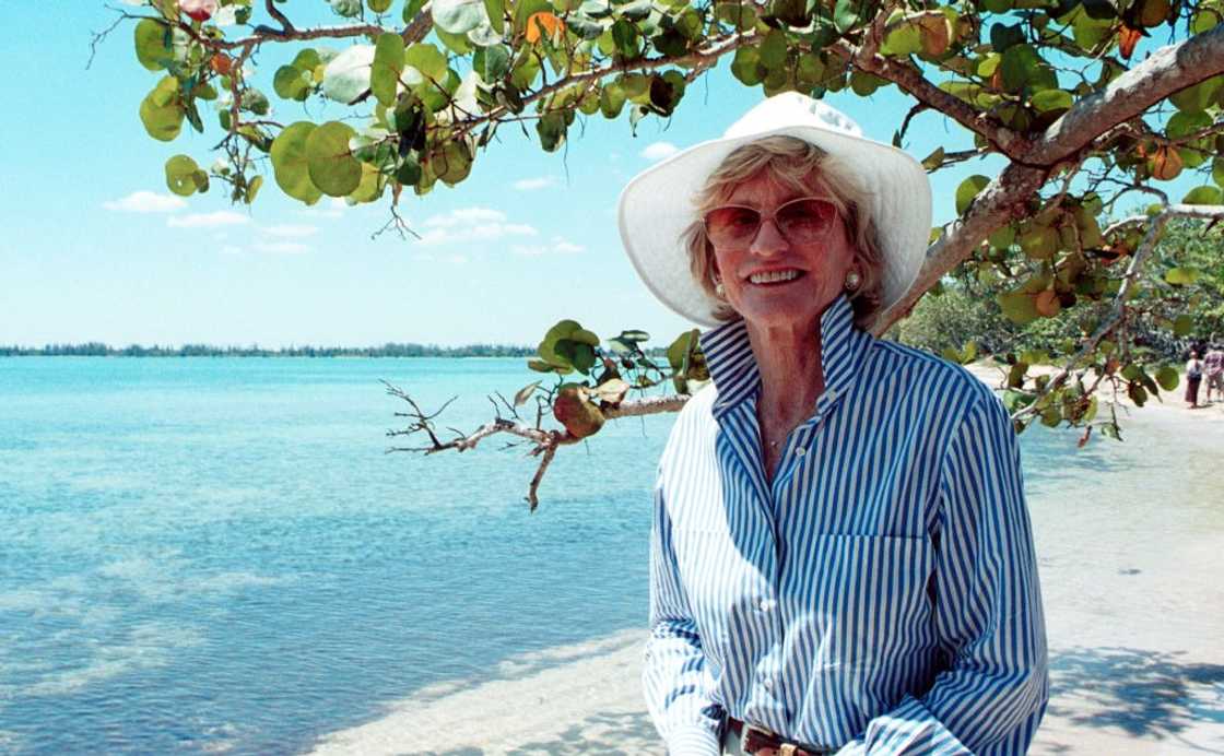 Jean Kennedy Smith in a striped shirt, white hat and sunglasses on the beach