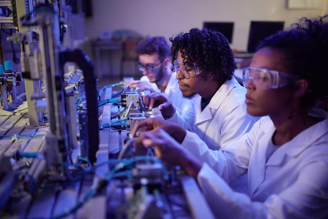 African American male scientist and his colleagues working on machinery in laboratory