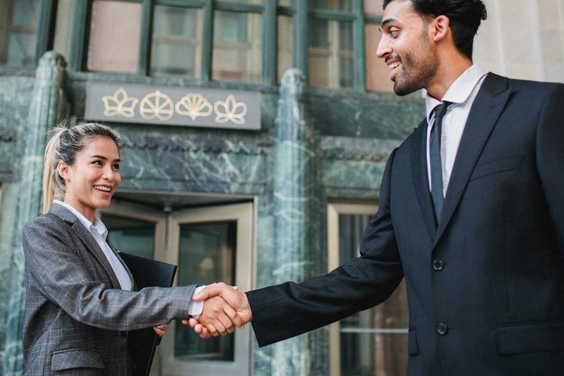 Two people smiling and shaking hands outside an office building.