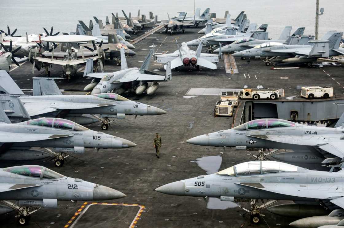 A US Navy officer walks past fighter jets parked on the flight deck of the USS Abraham aircraft carrier