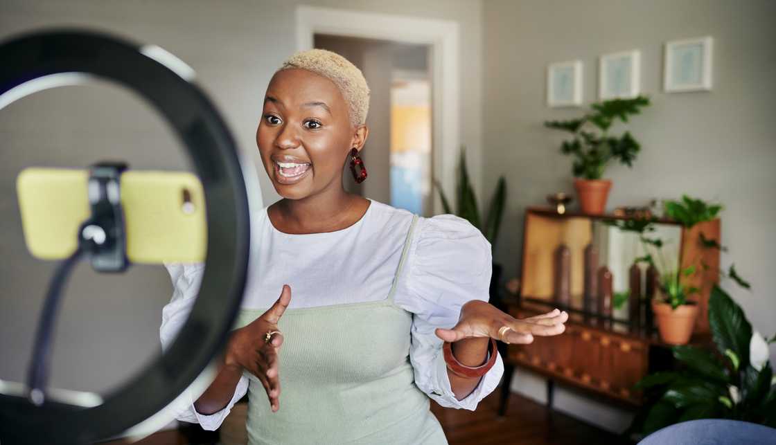 A smiling female influencer talks during a vlog post while standing in her living room A smiling female influencer talks during a vlog post while standing in her living room