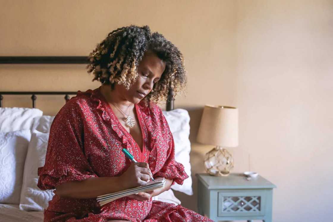 Woman sits on her bed writing in a journal Woman sits on her bed writing in a journal