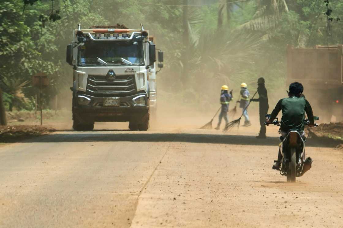 Workers armed with brooms, goggles, hats and scarves sweep an access road that carries 6,000 tonnes of ore destined for China each day