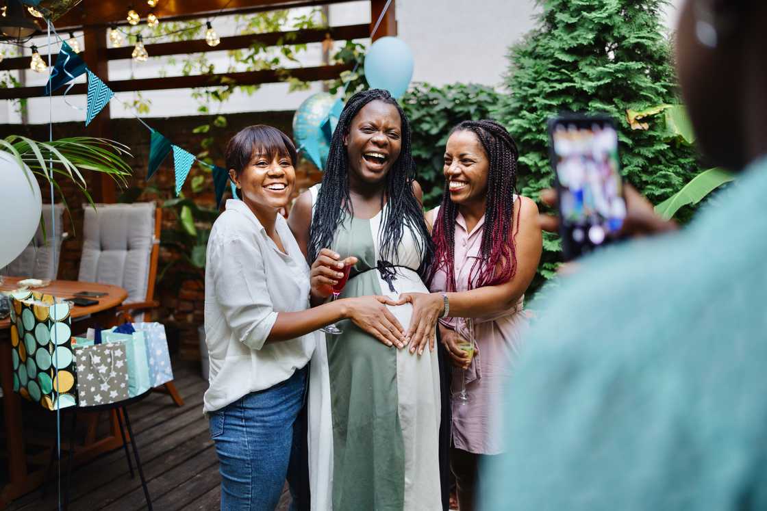 Three smiling women at a baby shower party in a backyard