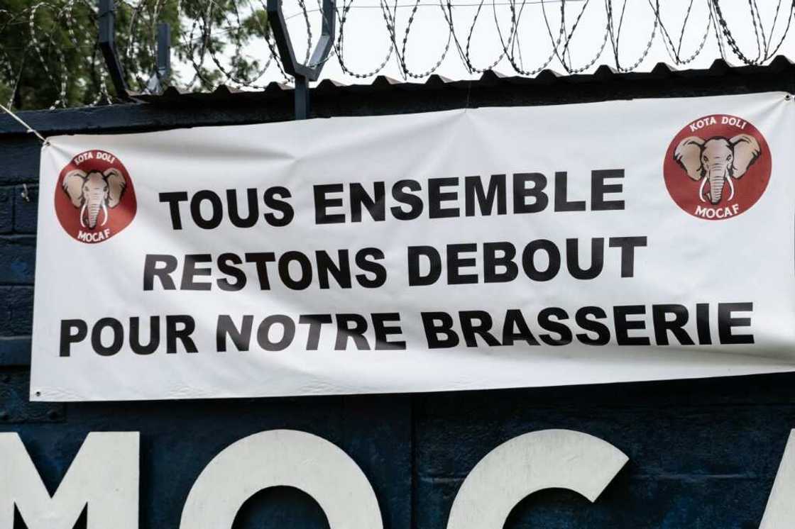 A sign on the brewery fence says 'Let's all stand together for our brewery'