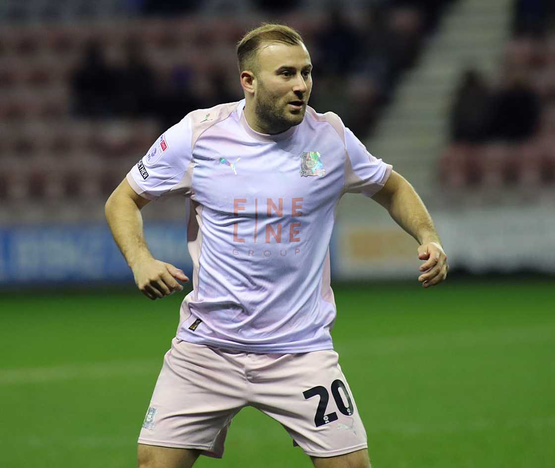 A footballer in a pink jersey numbered 20 runs on the field during a game.