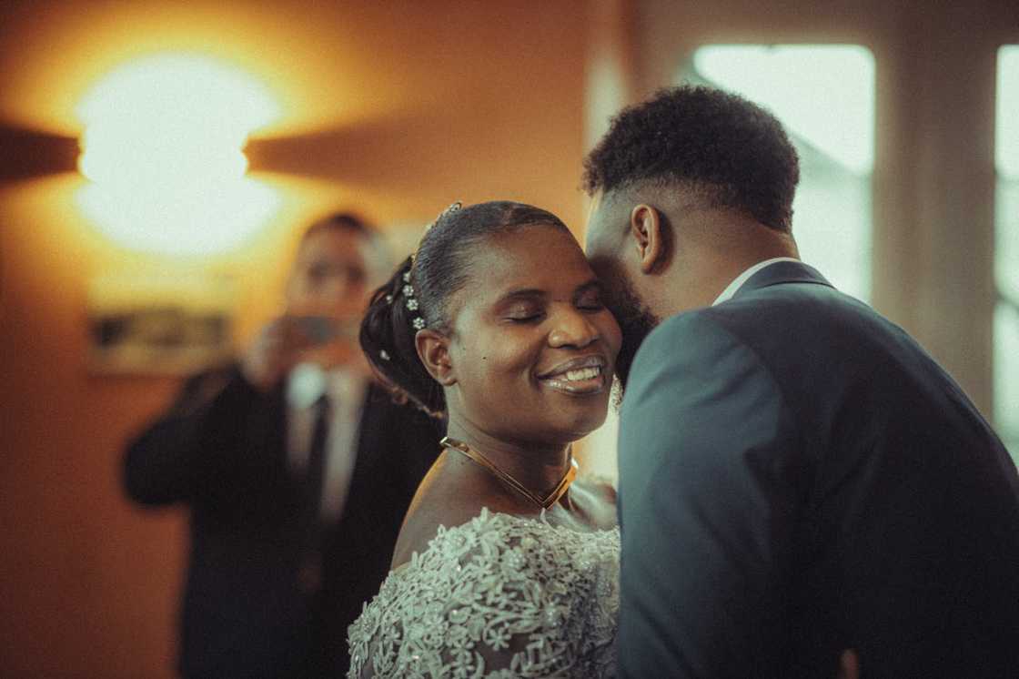 A bride smiles with eyes closed as groom leans in during their wedding dance.
