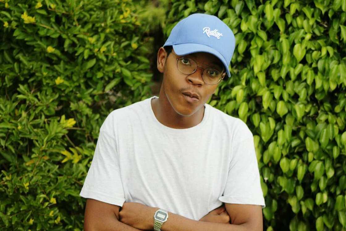 A young man standing in front of a green vegetation