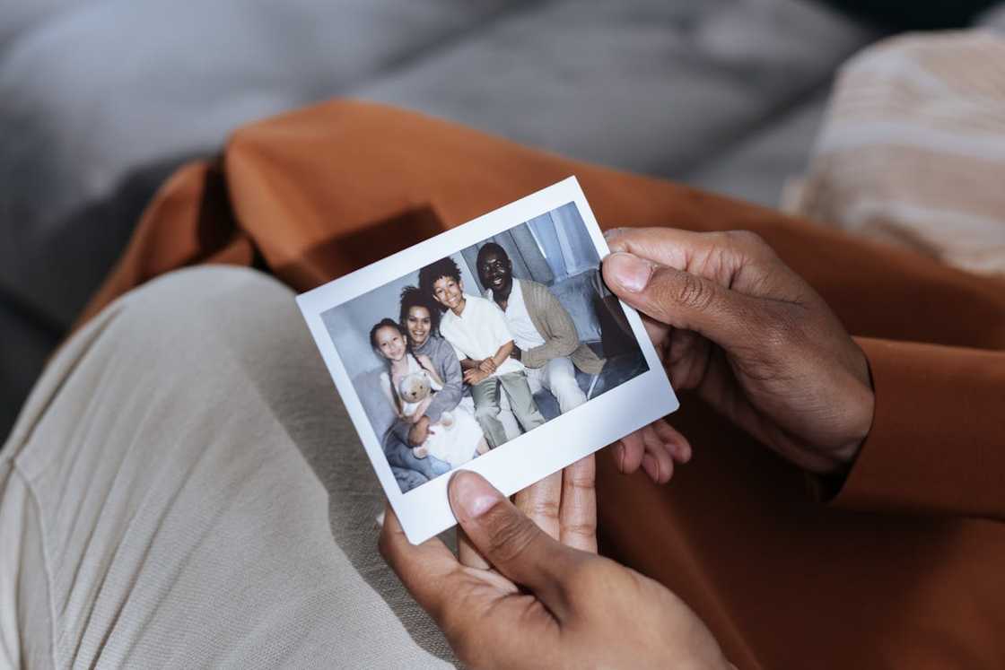 A person holds a small printed family photograph. A person holds a small printed family photograph.