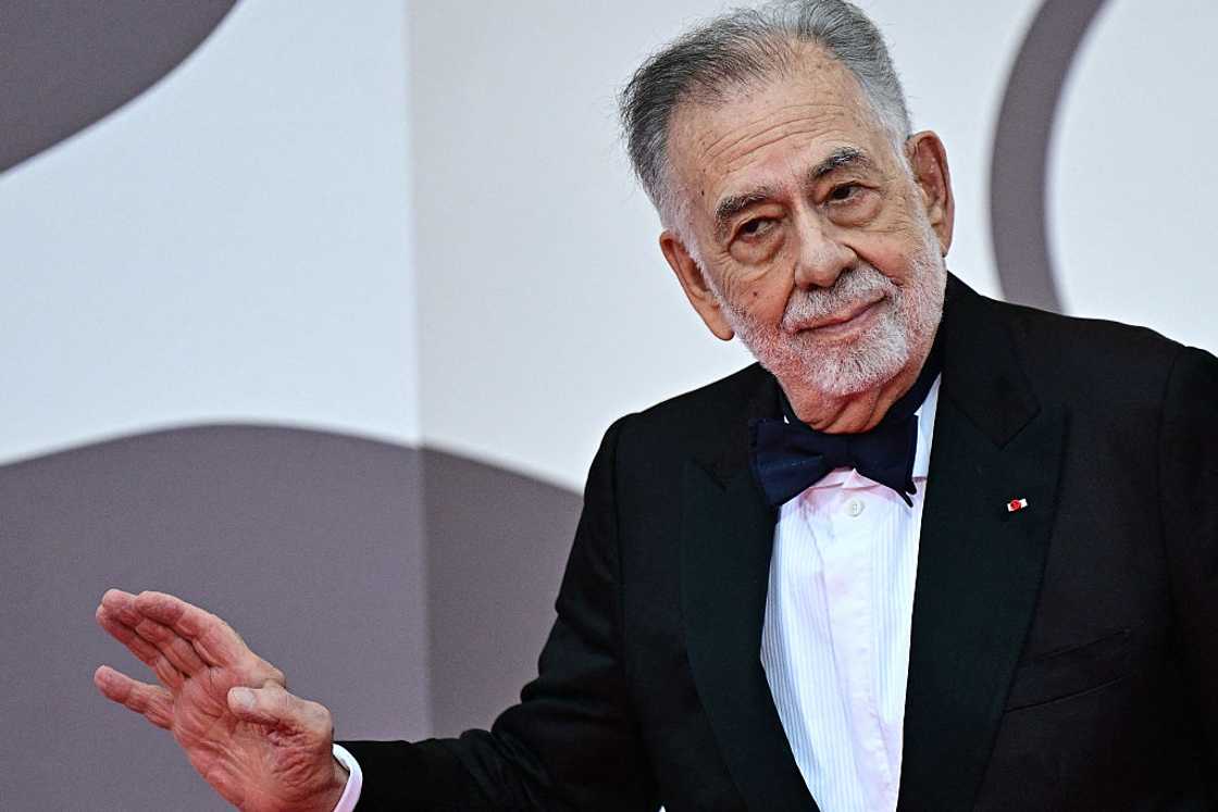 Francis Ford Coppola in a black tuxedo with a navy bow tie, gesturing with his hand while smiling on the red carpet. Francis Ford Coppola in a black tuxedo with a navy bow tie, gesturing with his hand while smiling on the red carpet.