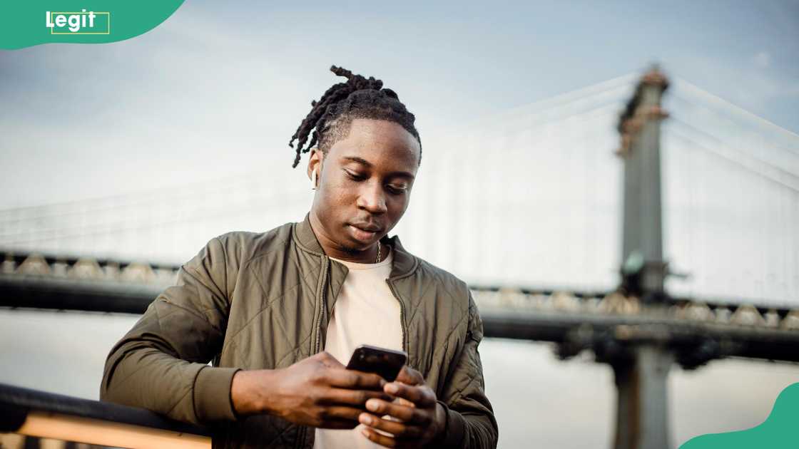 A man using his smartphone next to a bridge A man using his smartphone next to a bridge