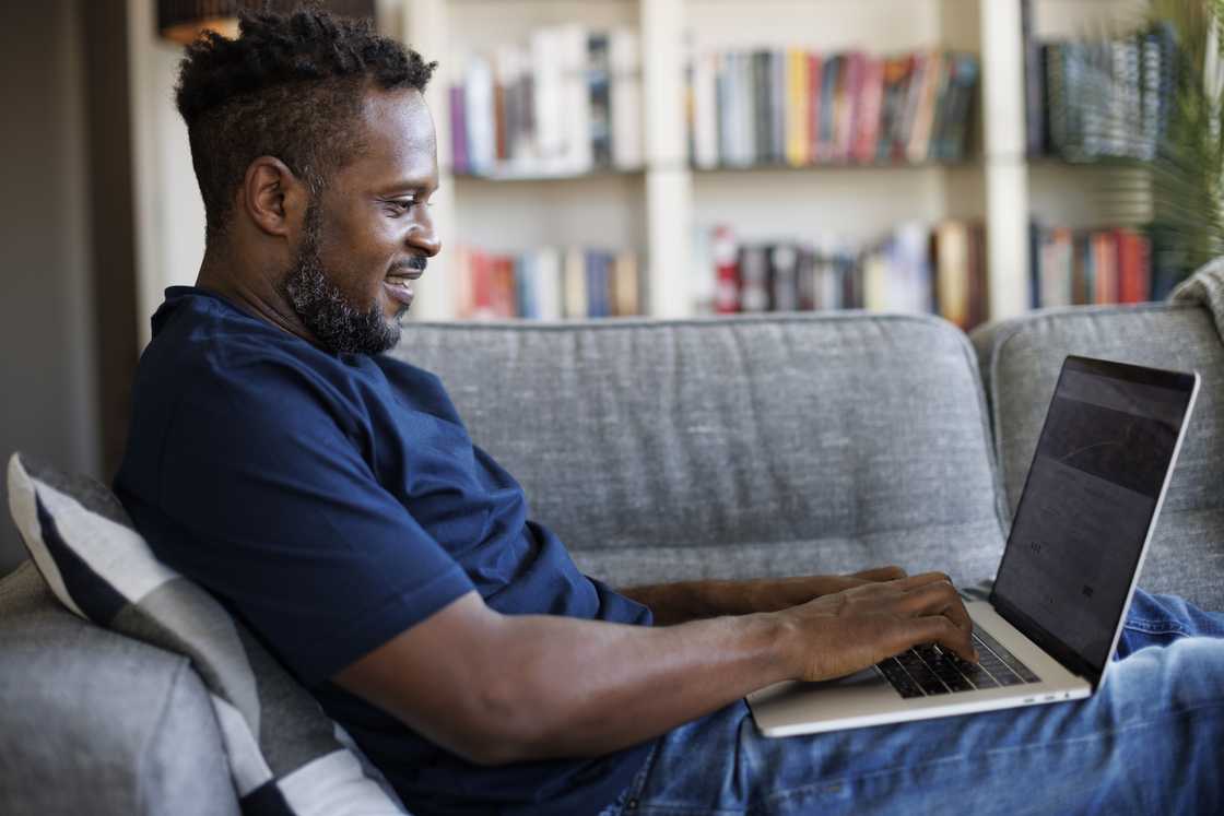 Relaxed smiling man sitting on sofa and using a laptop.