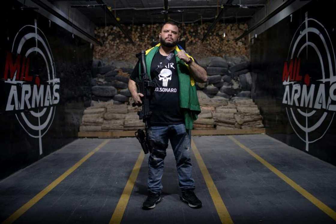 Former Military Police Major Elitusalem Gomes de Freitas, wearing a t-shirt bearing the name of Brazilian President Jair Bolsonaro, poses for a picture carrying his guns and the Brazilian flag, in the city of Nova Iguacu Former Military Police Major Elitusalem Gomes de Freitas, wearing a t-shirt bearing the name of Brazilian President Jair Bolsonaro, poses for a picture carrying his guns and the Brazilian flag, in the city of Nova Iguacu