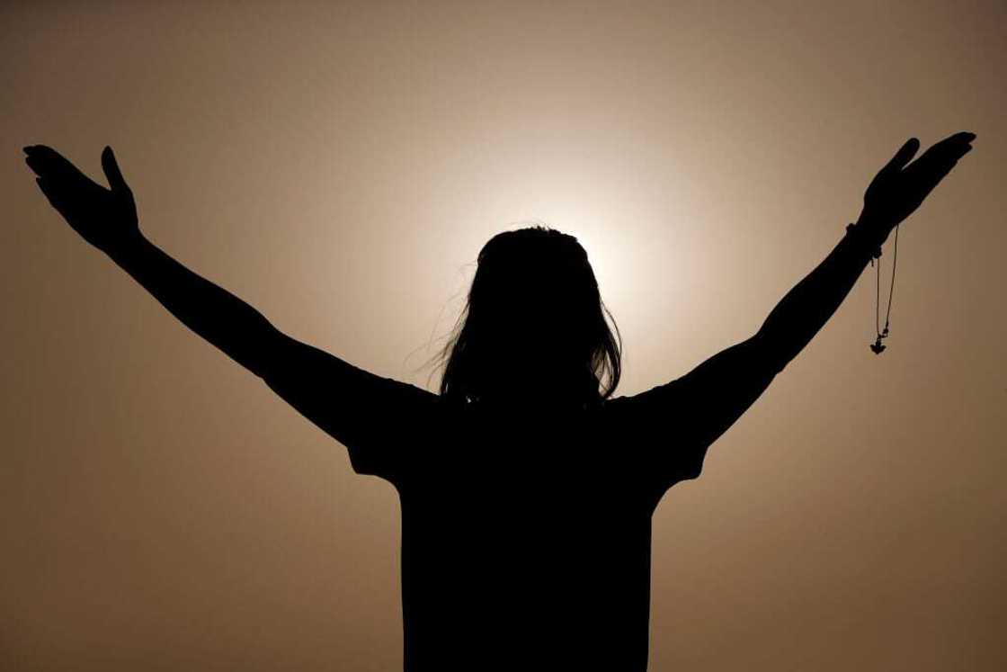 Silhouette of a woman praying with rosary beads at sunset