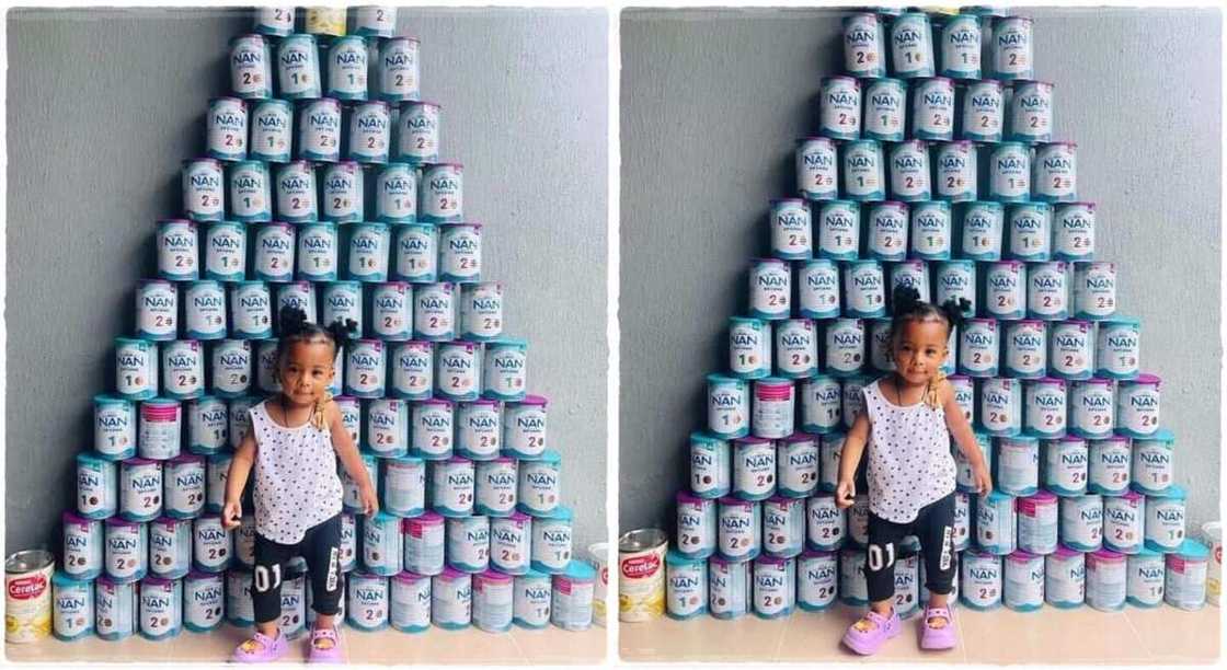 Photo of a baby girl standing in front of 87 cans of NAN milk.