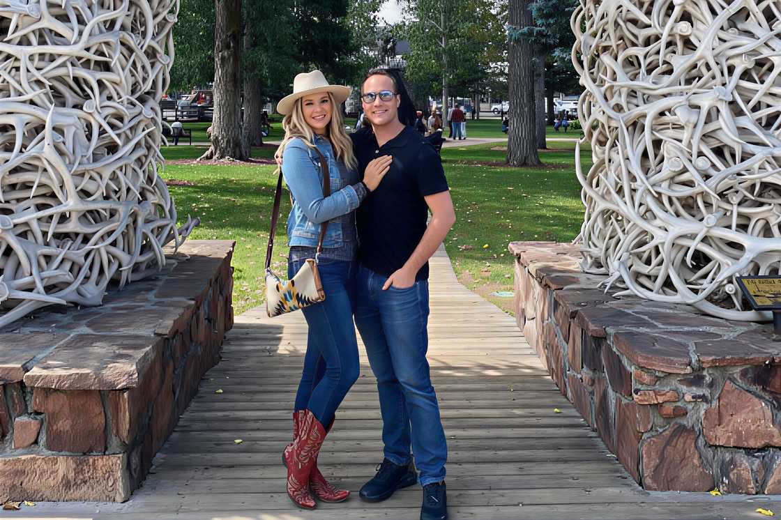 Katie Pavlich and Gavy Friedson pictured o‍n a woode‌n walkway between‌ two large elk antler arche⁠s