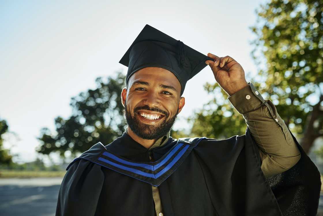 A young man smiles while holding his graduation cap A young man smiles while holding his graduation cap