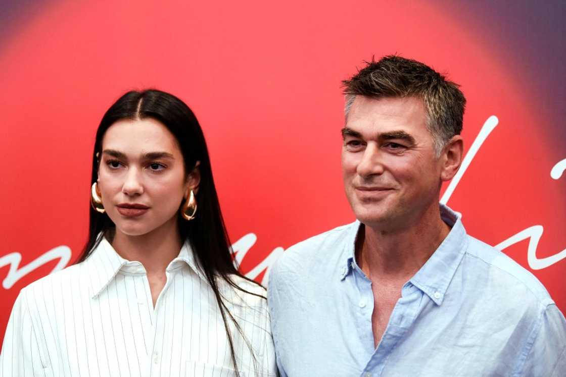 A woman in a white pinstriped shirt stands beside a man in a light blue button-up.