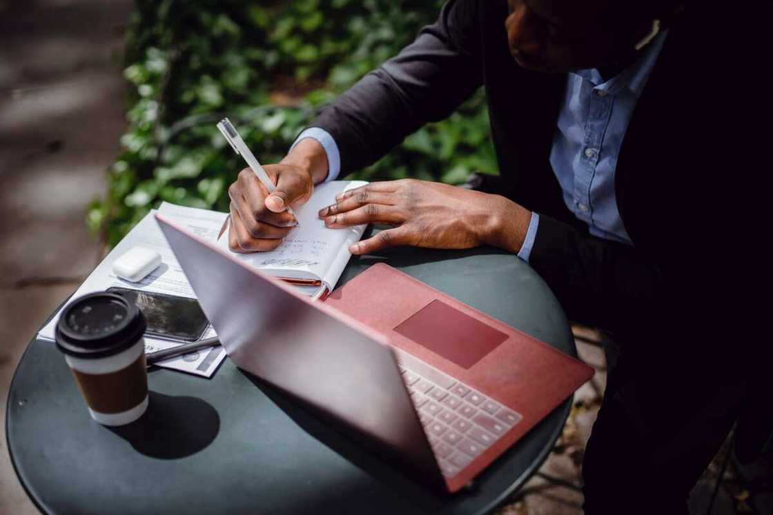 A man taking notes while using a laptop A man taking notes while using a laptop