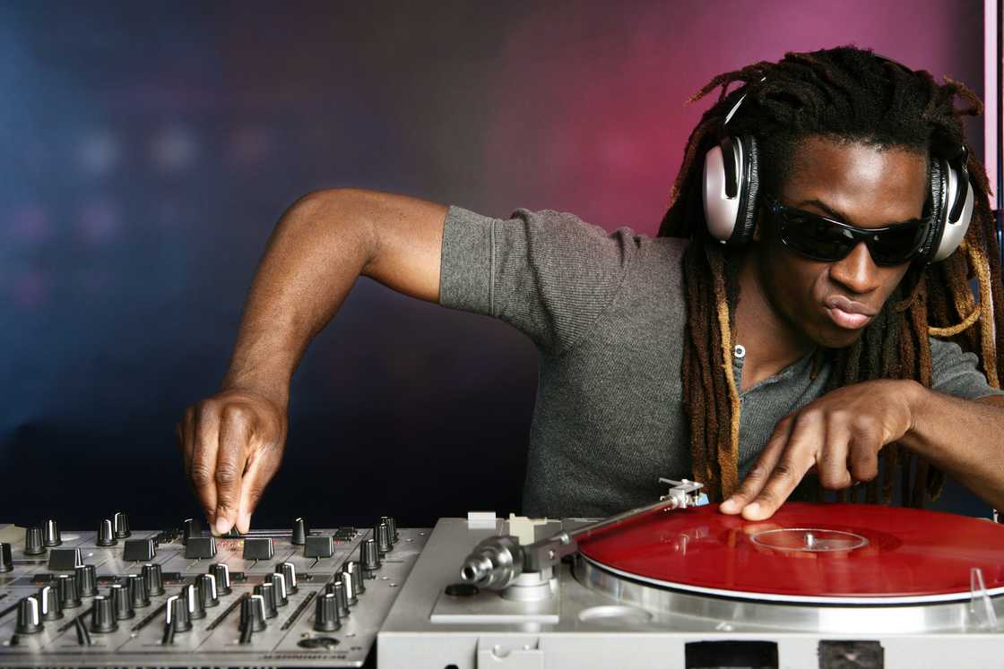 A person wearing headphones and sunglasses operates DJ equipment. A person wearing headphones and sunglasses operates DJ equipment.