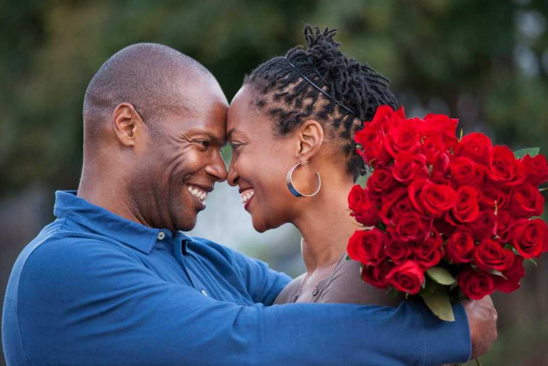 A man hugging his wife and giving her red roses