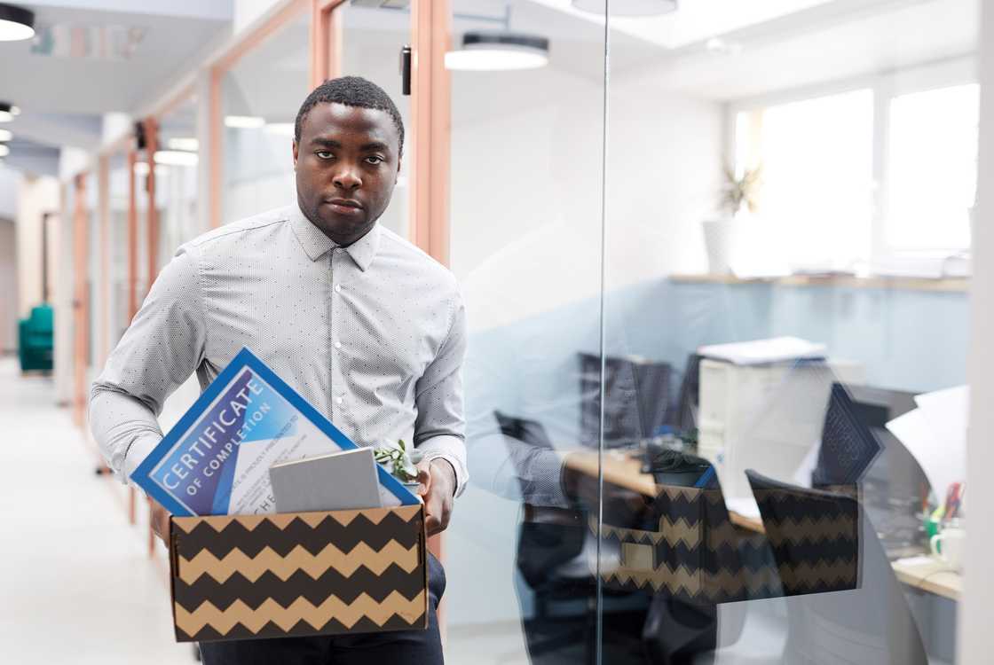 Corporate office exit scene, person holding box of belongings.