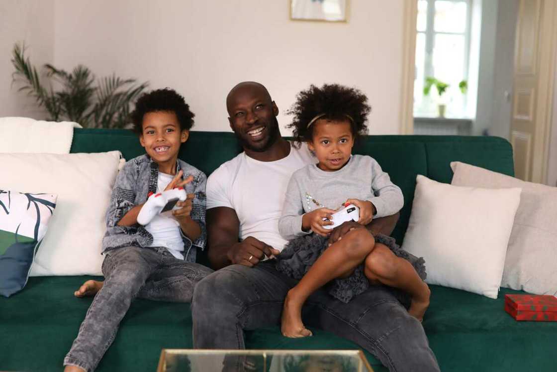 A young boy and girl playing PlayStation with their dad on a couch