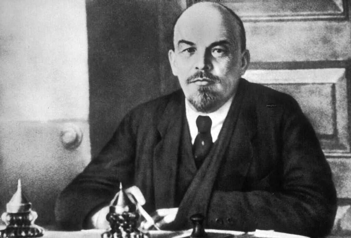 Vladimir Lenin sitting at a table in a black suit and a white shirt