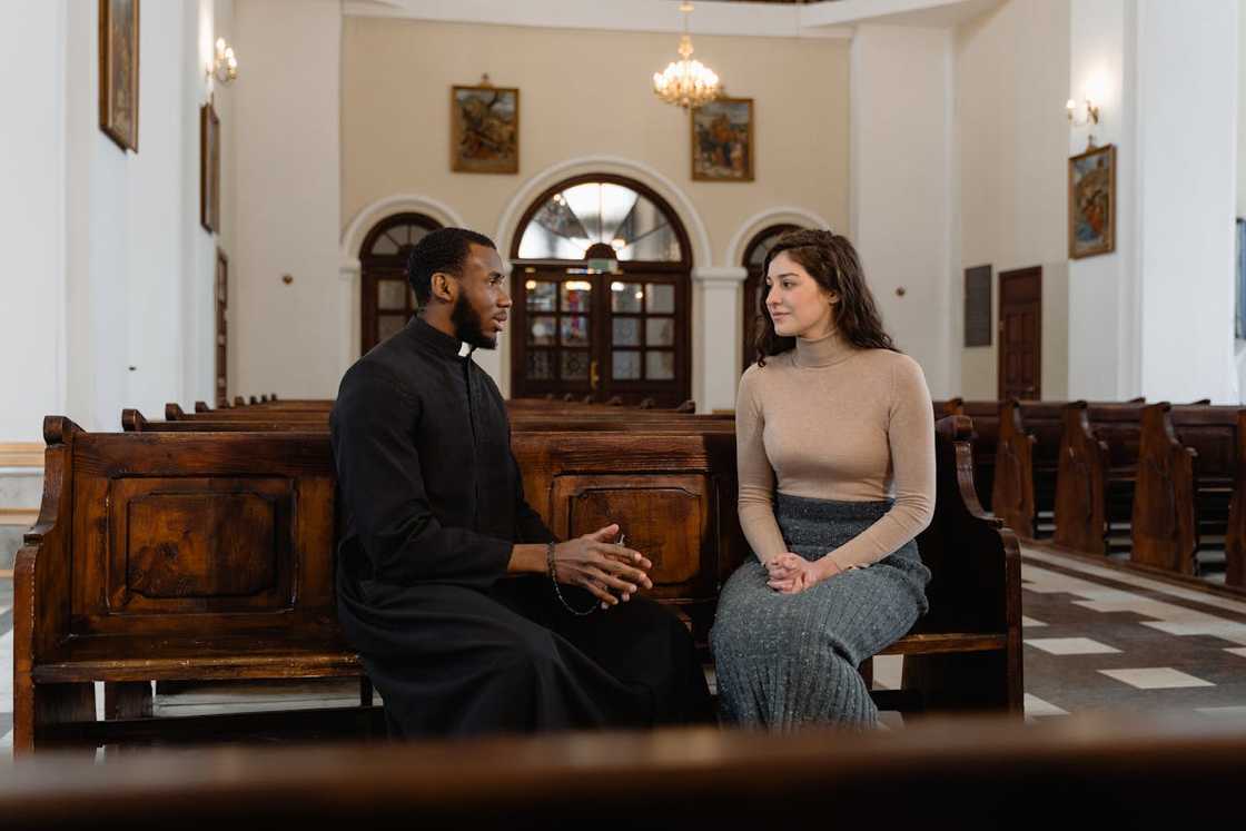 A pastor speaking privately with a woman while seated on church pews. A pastor speaking privately with a woman while seated on church pews.