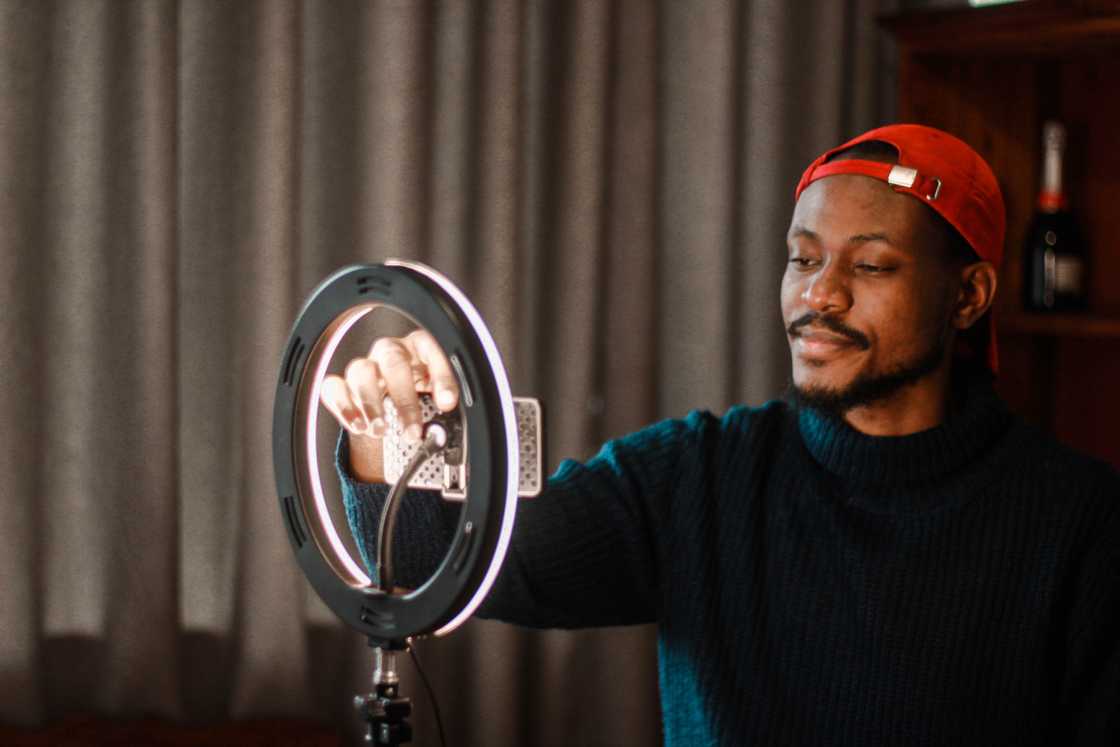 A man creating content using a ring-light and a smartphone. A man creating content using a ring-light and a smartphone.