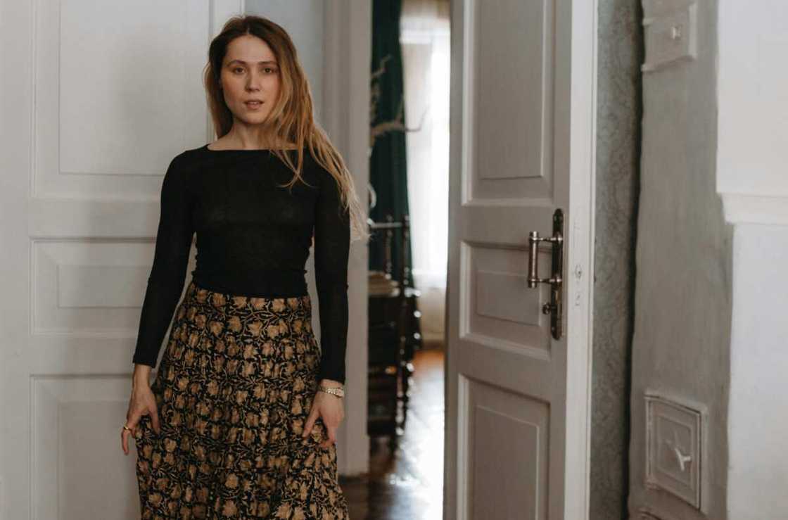 A woman walking in front of a door in a flowery skirt and a black top