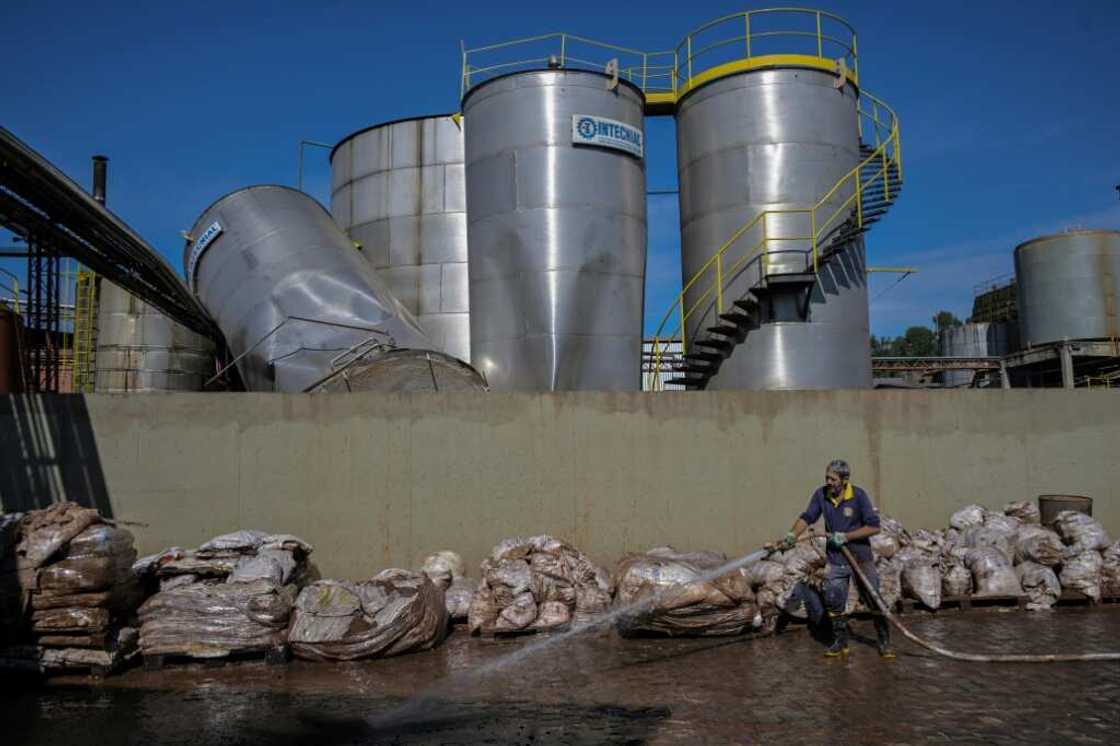 A worker uses a high pressure hose to remove mud accumulated by flooding at an industrial plant