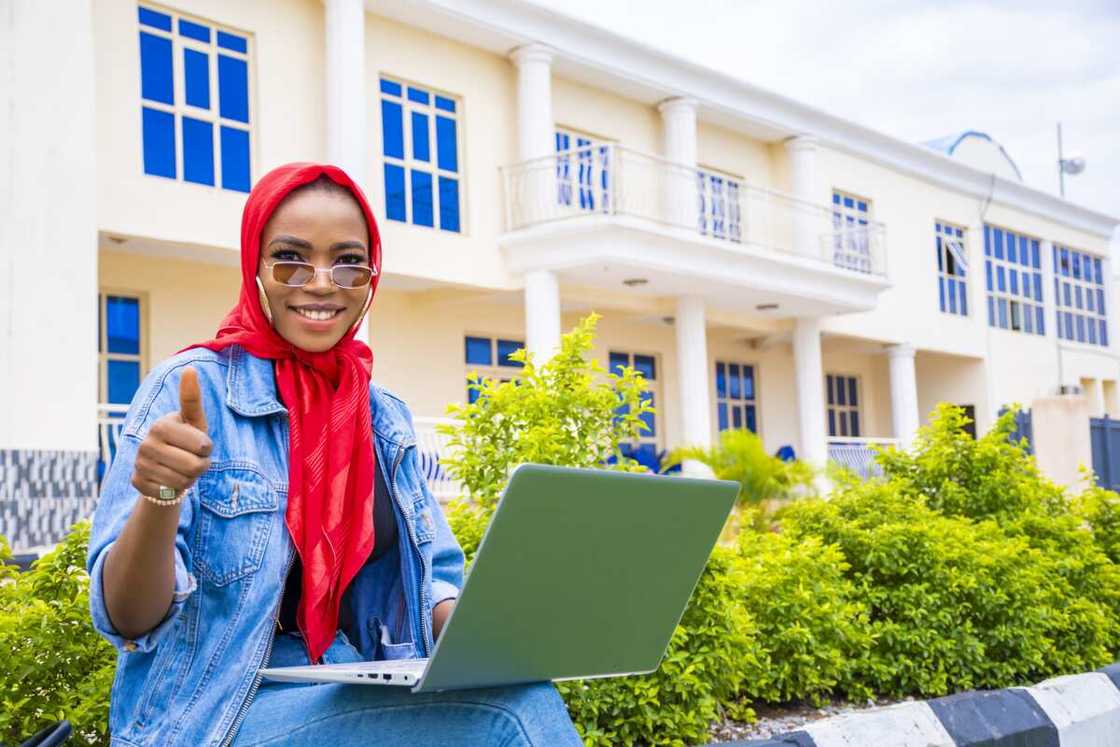 A female sitting in the park while holding her laptop A female sitting in the park while holding her laptop