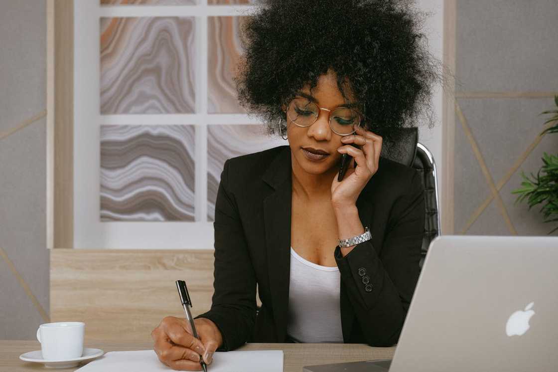 A woman talking on the phone while writing notes at a desk. A woman talking on the phone while writing notes at a desk.
