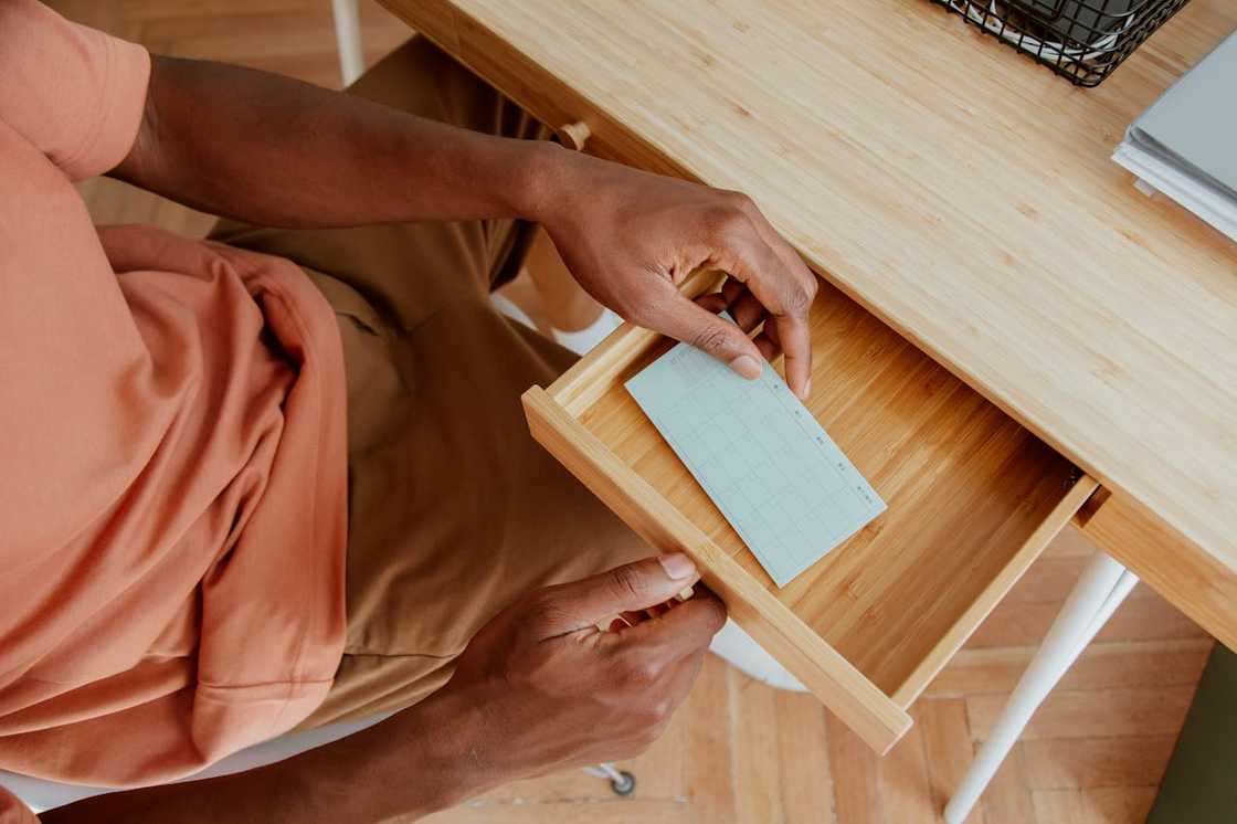 A person opening a desk drawer and taking out a small note card.