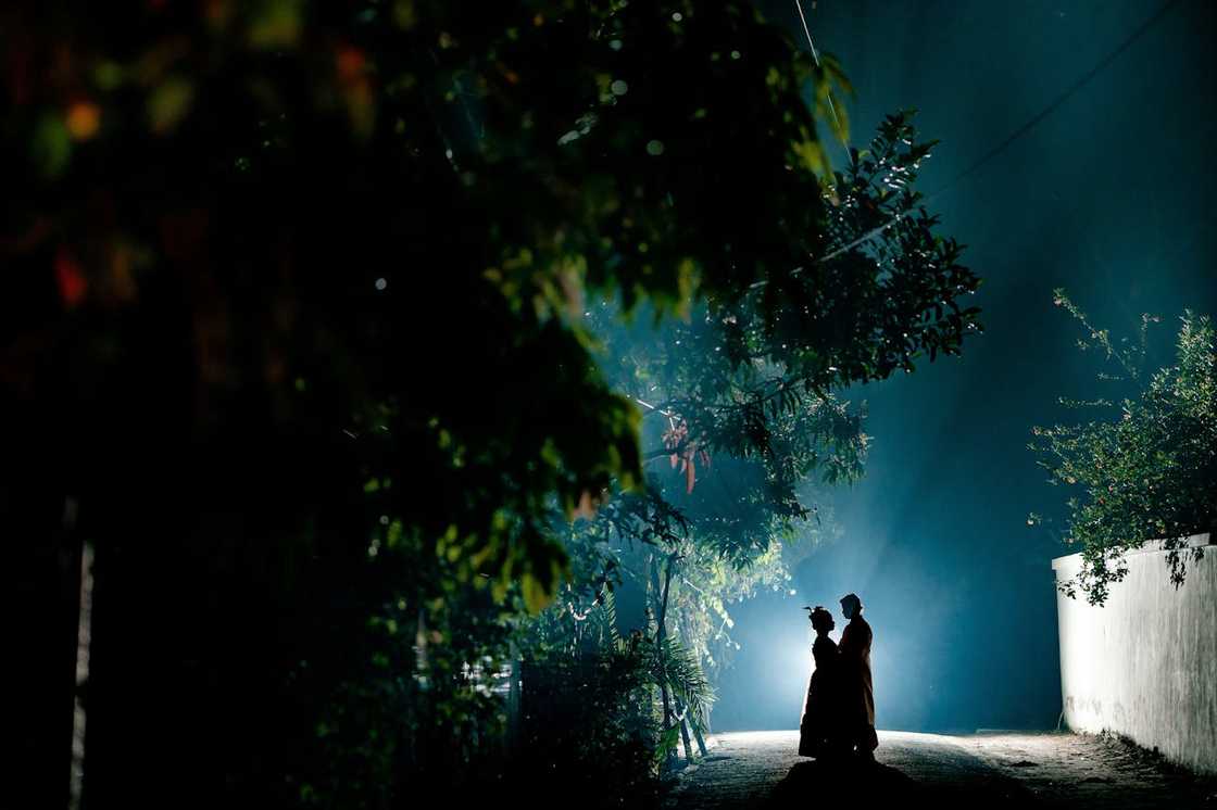 Two people standing in silhouette on a quiet road at night.