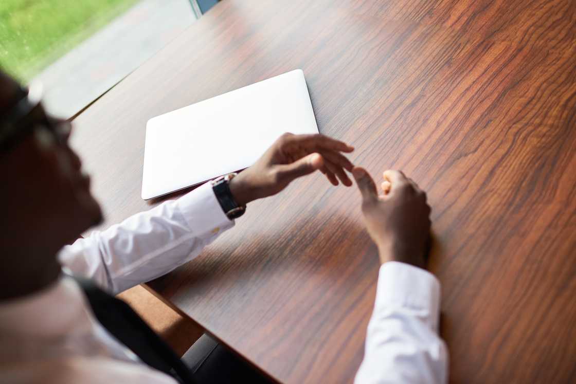 A hand adjusts a cufflink beside a brown envelope on a desk.
