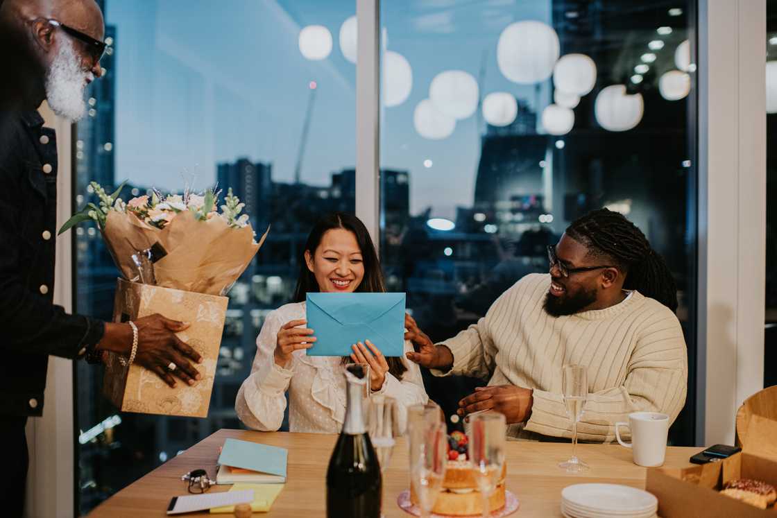 Colleagues gift a female employee a bouquet of flowers and a card at an after-work office party