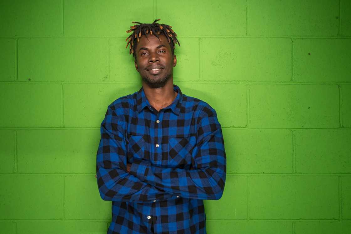 A man wearing a blue and black flannel shirt in front of a vivid green wall.