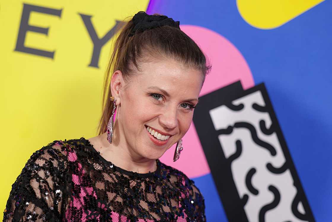 A woman with a high ponytail and sparkly earrings smiles in a black sequined mesh top. A woman with a high ponytail and sparkly earrings smiles in a black sequined mesh top.