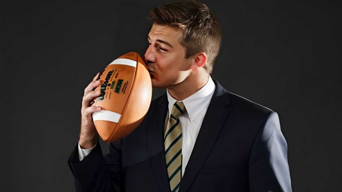 Austin Collinsworth poses standing kissing a football.