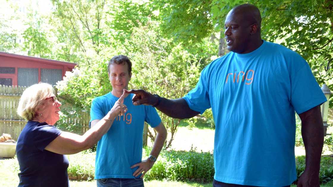 Ring founder Jamie Siminoff and Shaquille O'Neal are pictured with a homeowner sharing a 'Ring greeting' that mimics the ringing of a doorbell.