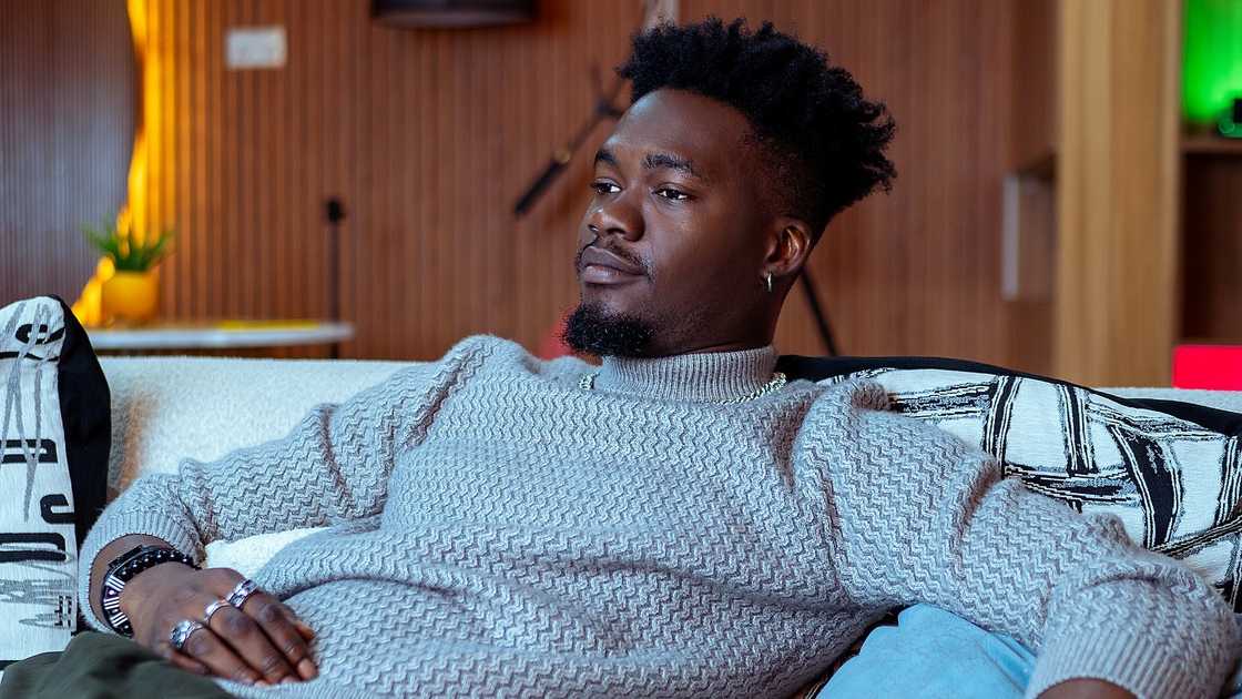 Jason Jae from BBNaija relaxes on a white couch.