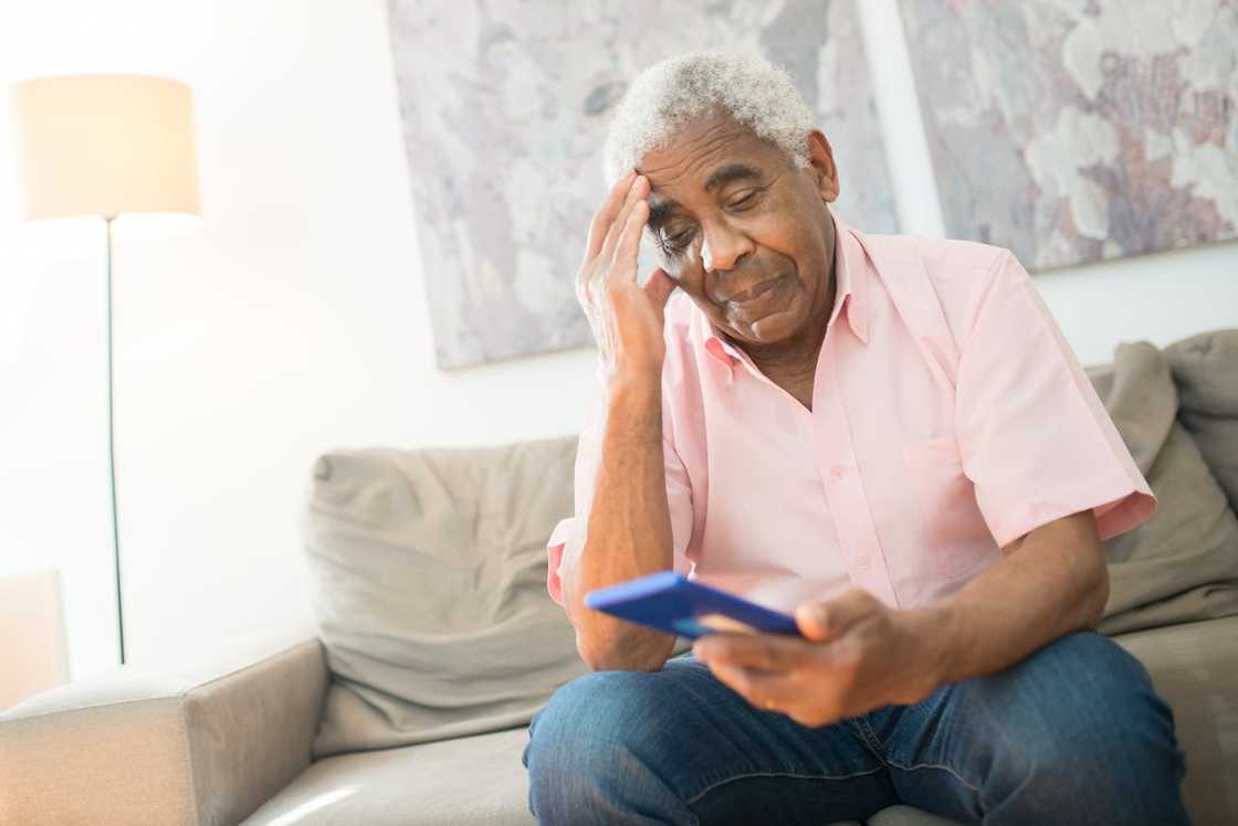 Elderly man sitting on a sofa looking worried while checking his phone. Elderly man sitting on a sofa looking worried while checking his phone.