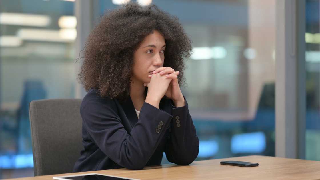 Person sits at a conference table with hands clasped near face. Person sits at a conference table with hands clasped near face.