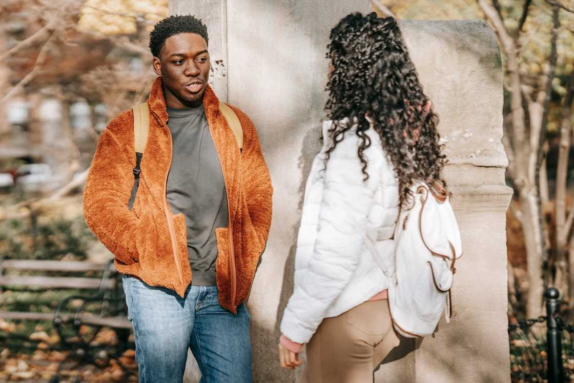 Two people stand outdoors and talk near a stone wall. Two people stand outdoors and talk near a stone wall.