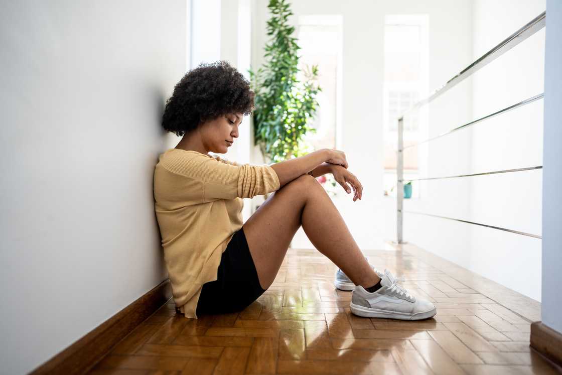 Sad young woman sitting on ground at home