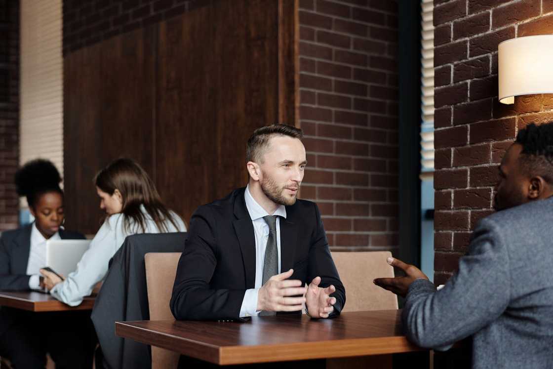 Two men talk across a table in a café during a business meeting. Two men talk across a table in a café during a business meeting.