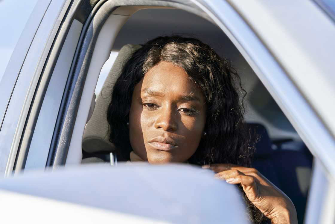 A woman stares outside her car